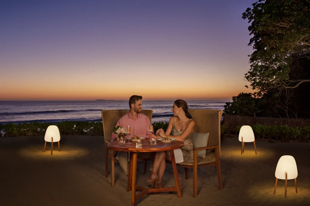 Couple dining on the beach at sunset with candle lighting at Dreams Bahia Mita.