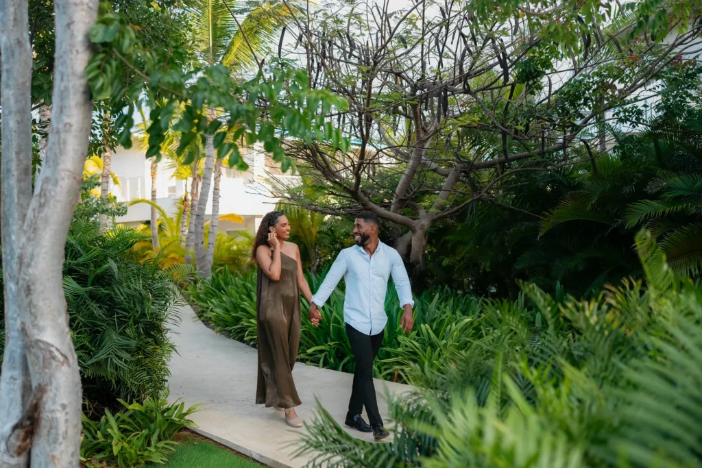 Couple walking hand in hand through lush tropical gardens at Dreams Cap Cana Resort & Spa.