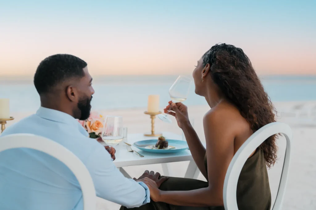 Couple enjoying a romantic beachfront dinner with wine at sunset at Dreams Cap Cana Resort & Spa.
