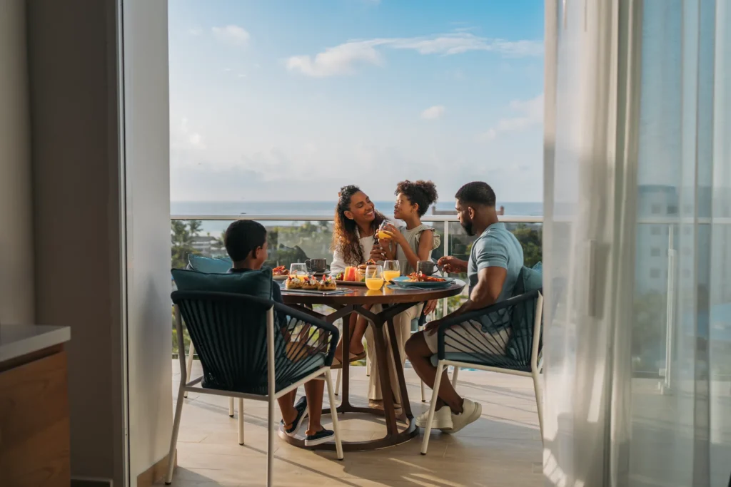 Family dining together on a private balcony with ocean views at Dreams Cap Cana Resort & Spa.