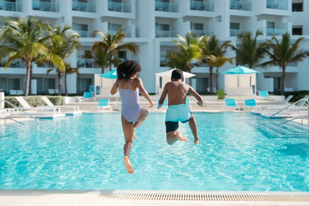 Children jumping into a resort pool at Dreams Cap Cana Resort & Spa with tropical surroundings.