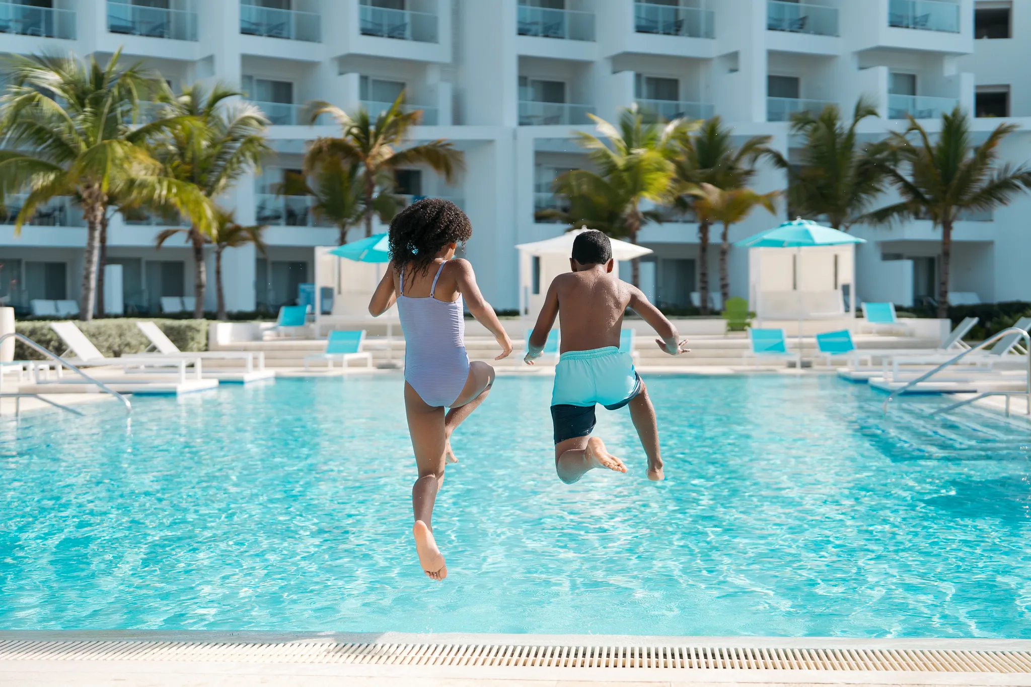 Children jumping into a resort pool at Dreams Cap Cana Resort & Spa with tropical surroundings.
