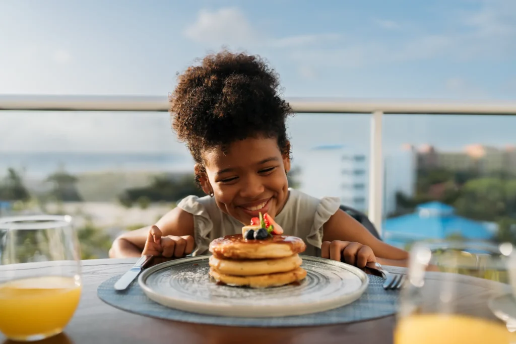 Child smiling at a plate of pancakes during breakfast at Dreams Cap Cana Resort & Spa in Punta Cana.