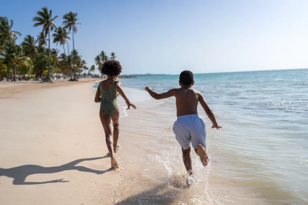 Children running along a tropical beach at Dreams Cap Cana Resort & Spa, enjoying a fun family vacation in Punta Cana.