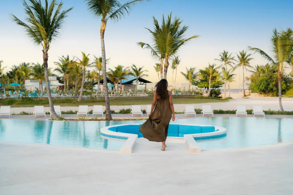 Guest walking toward a pool lounge area surrounded by palm trees at Dreams Cap Cana Resort & Spa.