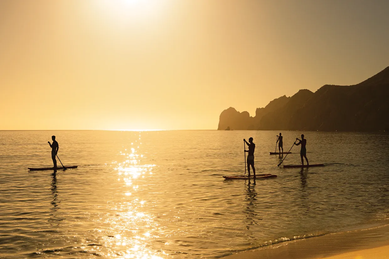 Guests paddleboarding along the Cabo shoreline at sunset near Breathless Cabo San Lucas.