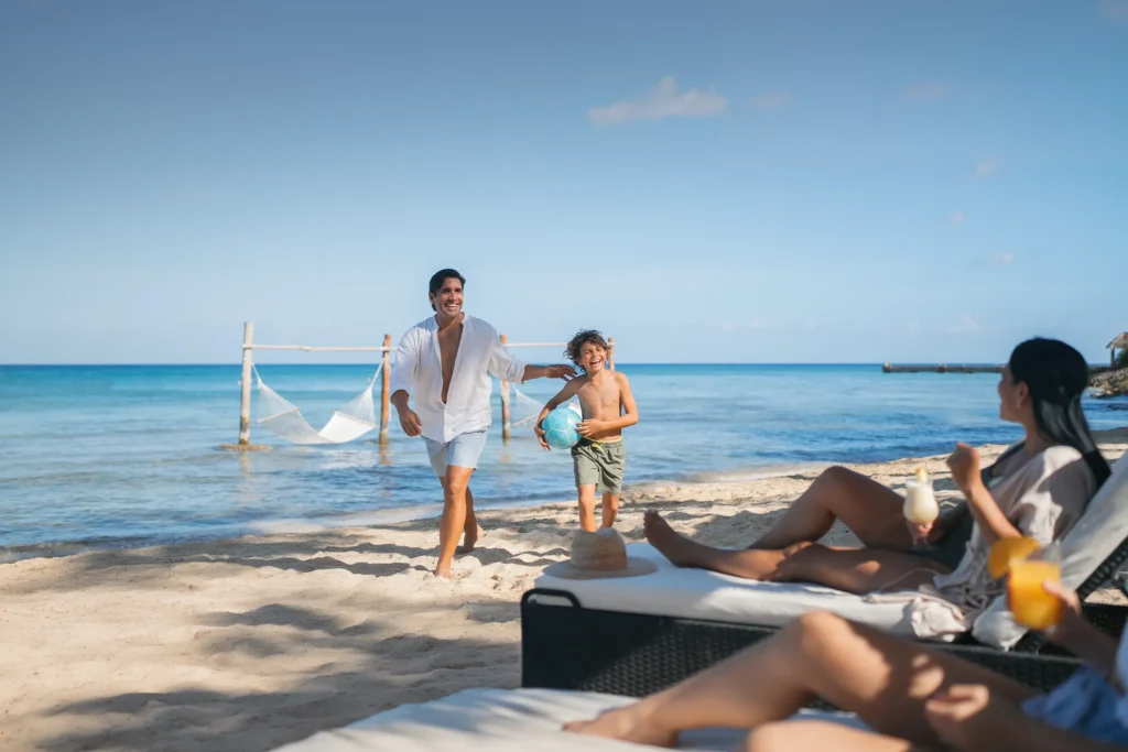 Family playing on the beach at Dreams Cozumel Cape Resort & Spa with ocean hammocks in the background.