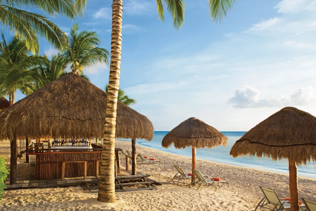 Sugar Reef beach bar at Dreams Cozumel Cape Resort & Spa featuring thatched palapas, tropical cocktails, and oceanfront seating on the sandy beach.