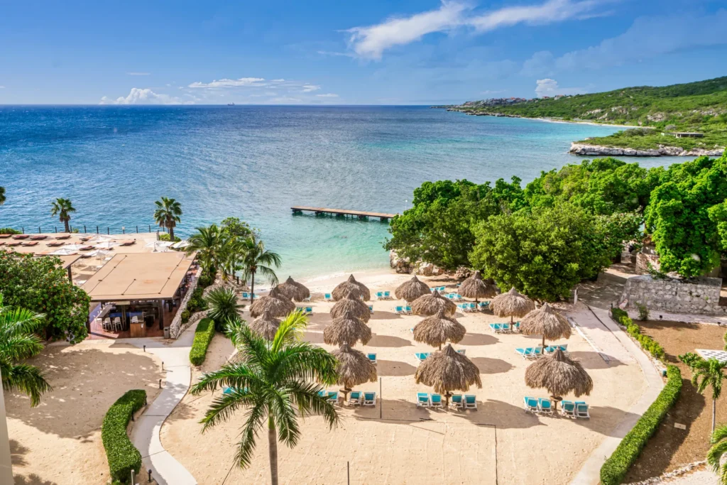 Sandy beach with palapa umbrellas and lounge chairs at Dreams Curaçao Resort.