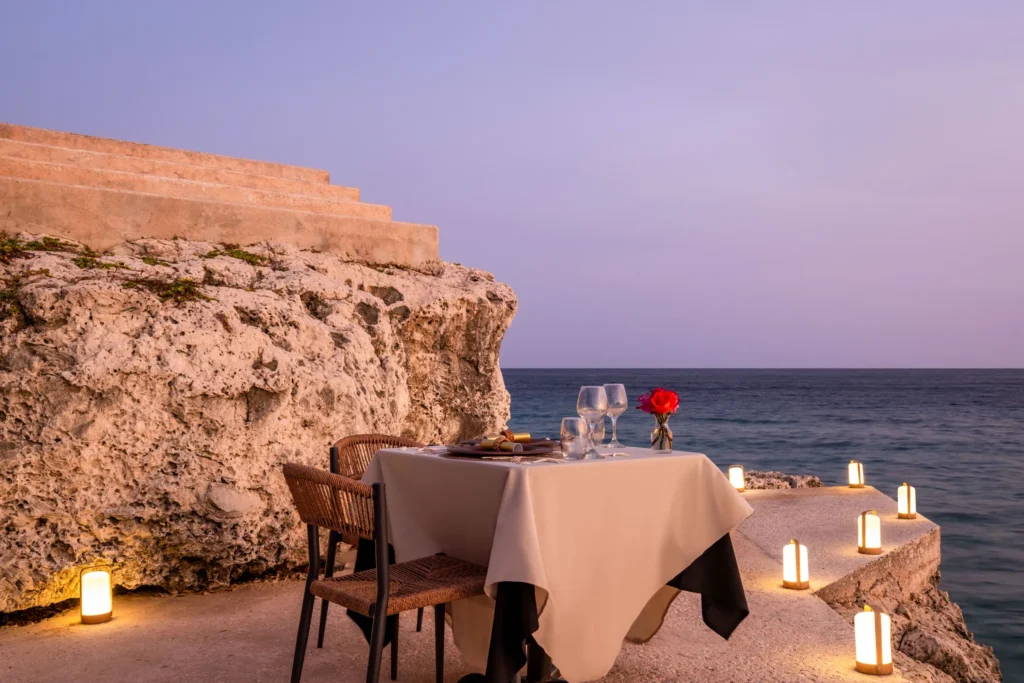 Romantic private dinner setup on a cliff overlooking the ocean at sunset at Dreams Curaçao Resort.