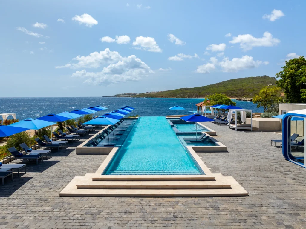 Luxury infinity pool with blue umbrellas overlooking the ocean at Dreams Curaçao Resort.