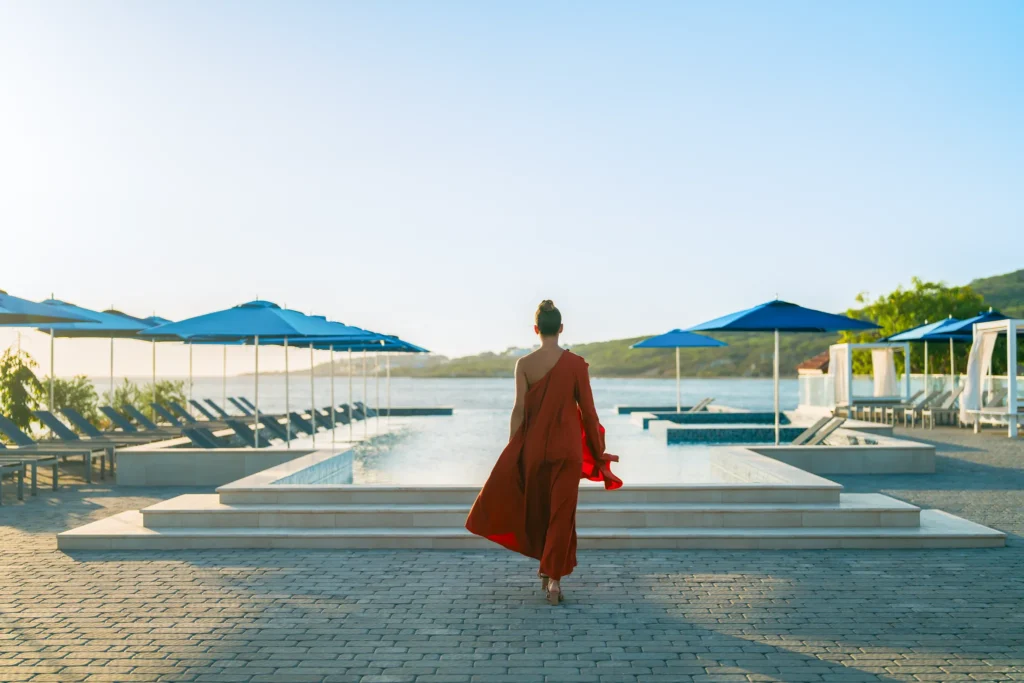 Woman walking toward infinity pool with ocean views at Dreams Curaçao Resort.