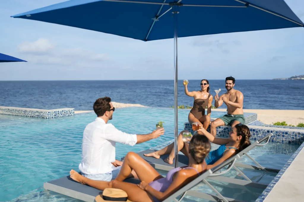 Friends relaxing with cocktails in an oceanfront infinity pool at Dreams Curaçao Resort.