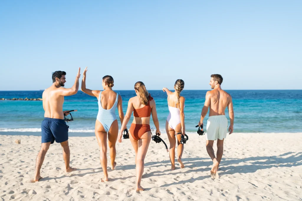 Friends walking toward the ocean with snorkeling gear at Dreams Curaçao Resort.