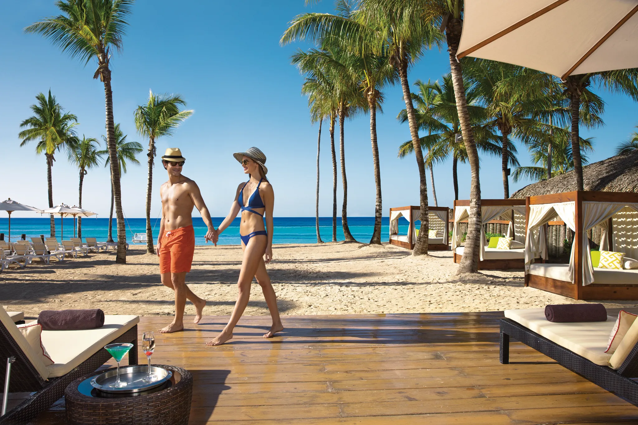 Couple walking hand in hand along the palm-lined beach at Dreams Dominicus La Romana Resort.