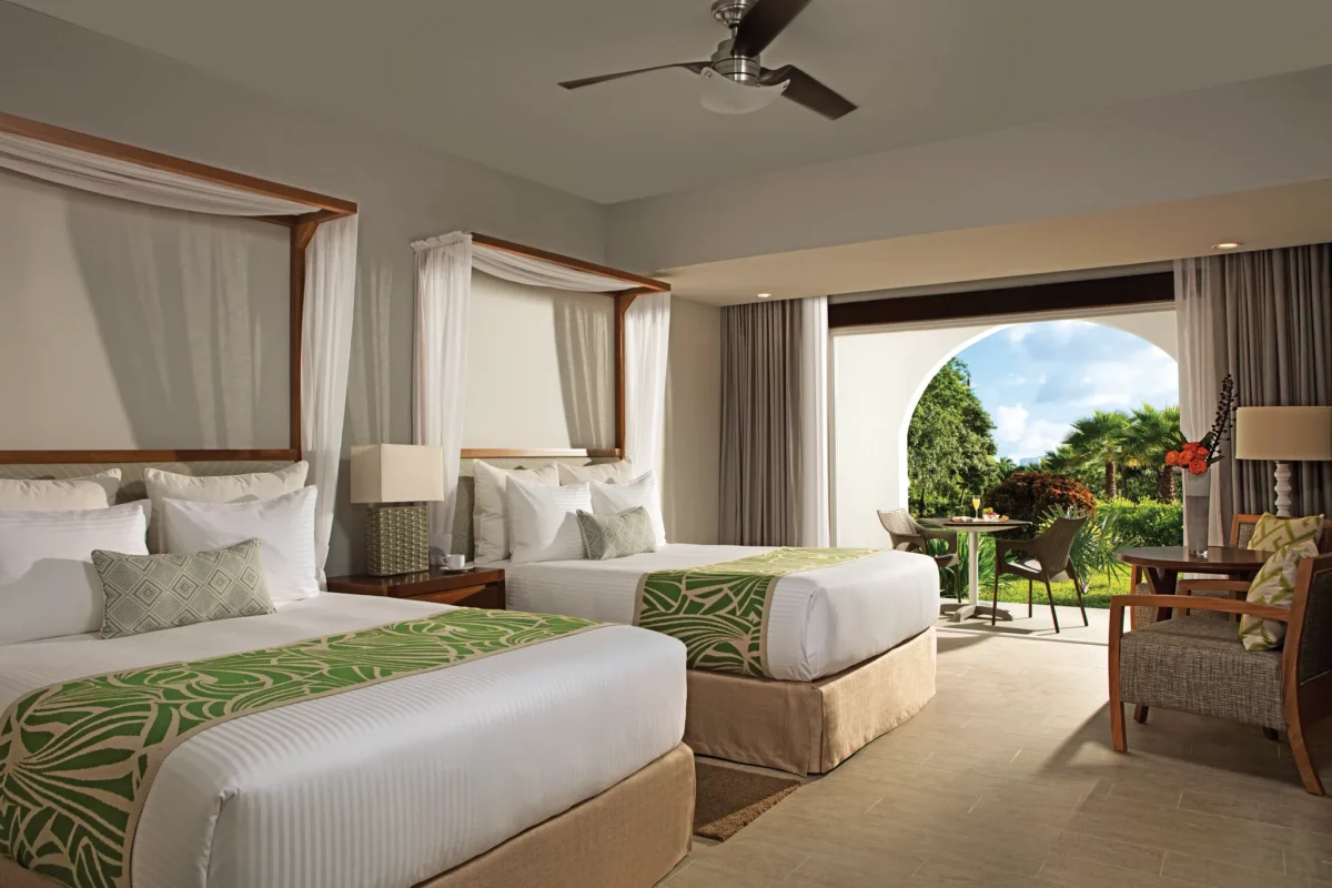 Deluxe Tropical View room with two double beds and furnished terrace at Dreams Dominicus La Romana overlooking lush gardens.