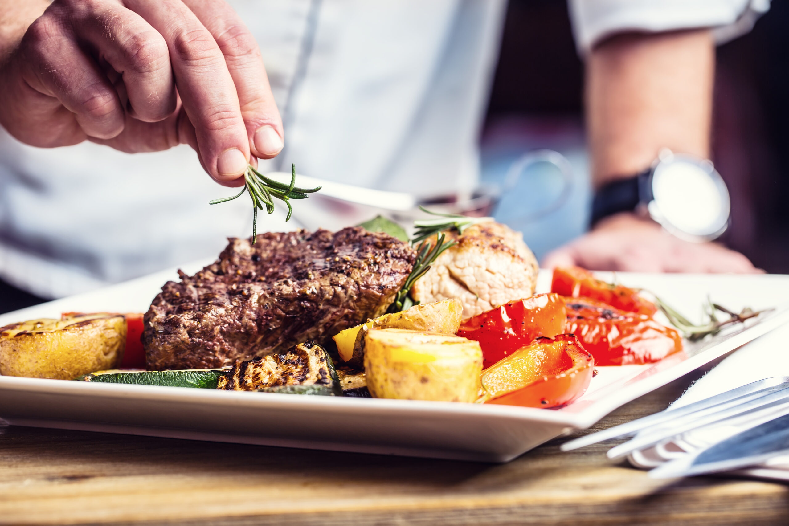 Chef in hotel or restaurant kitchen cooking only hands. Prepared beef steak with vegetable decoration.