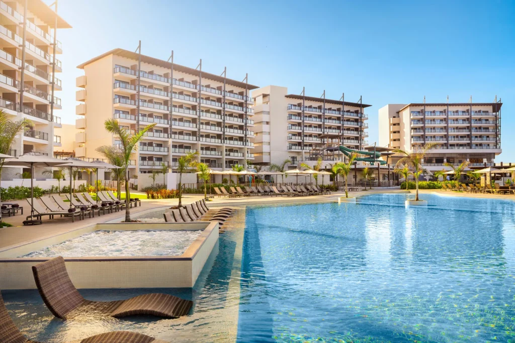 Large resort pool surrounded by lounge chairs and palm trees at Dreams Estrella del Mar Mazatlan Golf & Spa Resort.