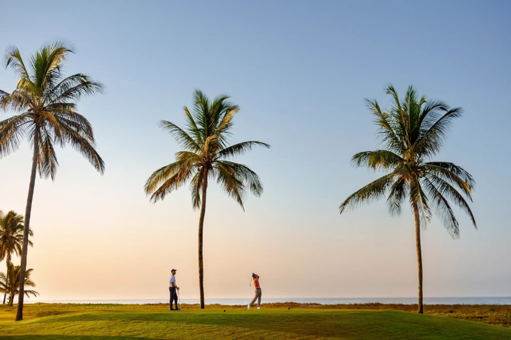 Golfers playing on a palm-lined oceanfront golf course at Dreams Estrella del Mar Mazatlan Golf & Spa Resort.