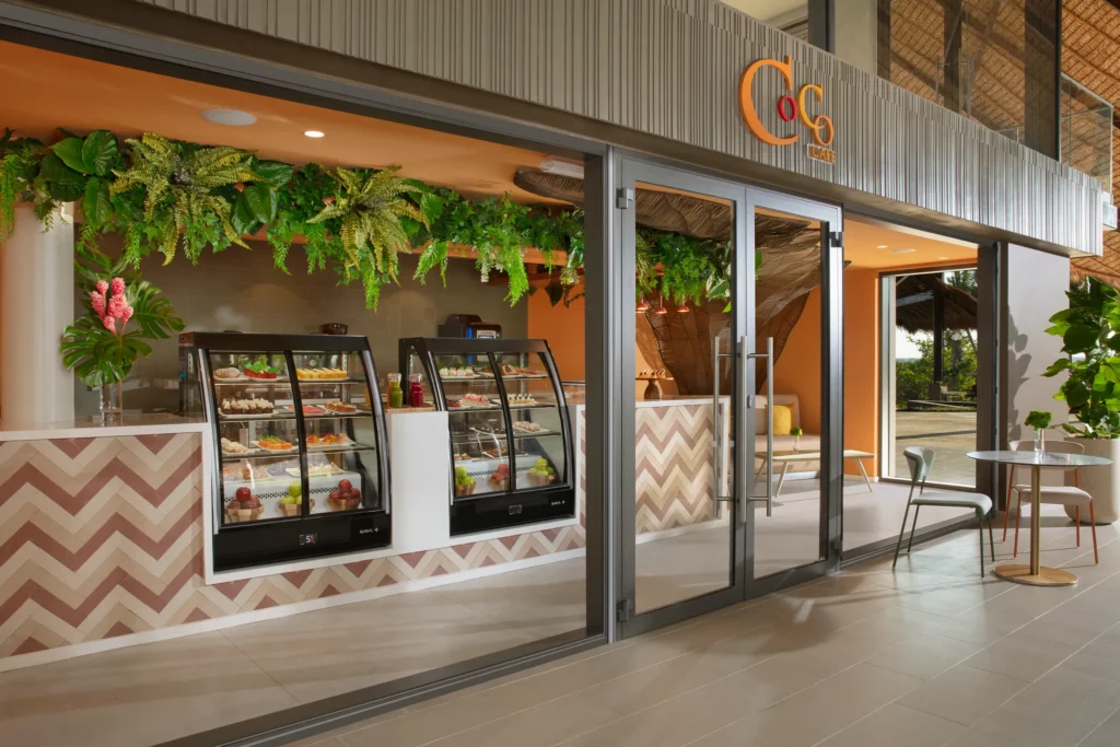 Coco Café at Dreams Flora Resort & Spa featuring a modern coffee shop with pastry displays, fresh desserts, and indoor-outdoor seating.
