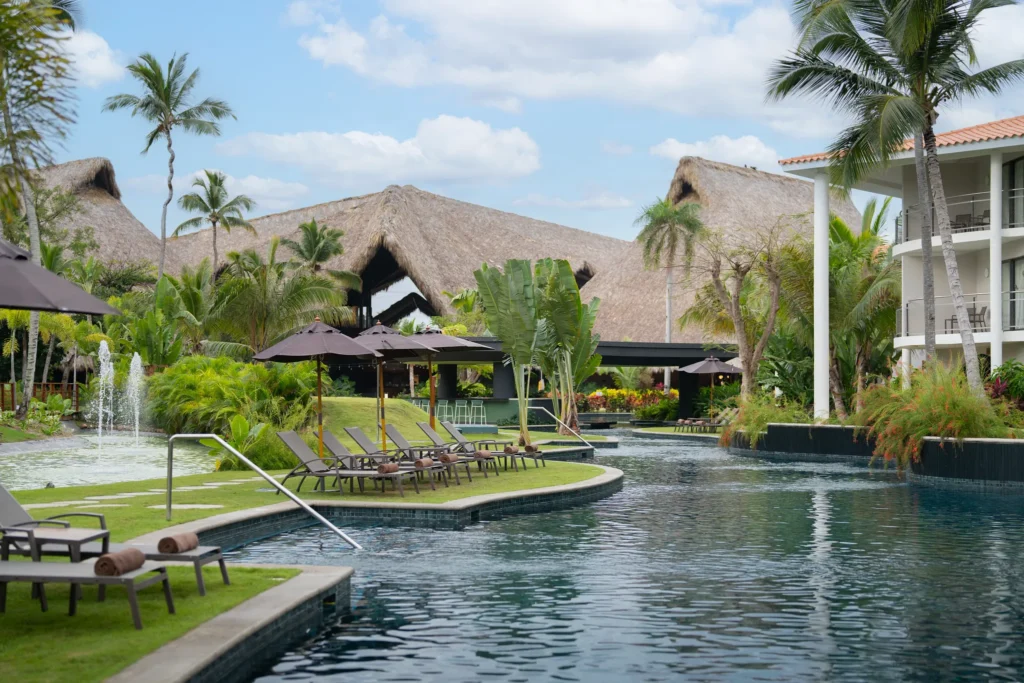 Lagoon-style pool with loungers and tropical landscaping near lobby at Dreams Flora Resort & Spa Punta Cana.