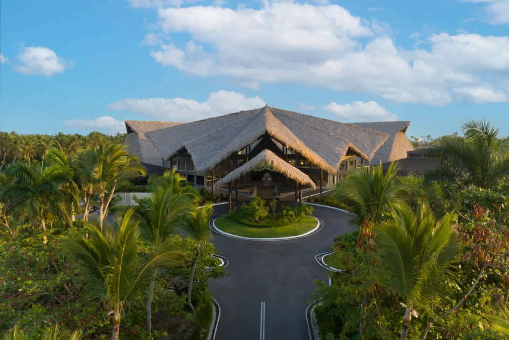 Grand entrance with thatched-roof lobby surrounded by palm trees at Dreams Flora Resort & Spa Punta Cana.
