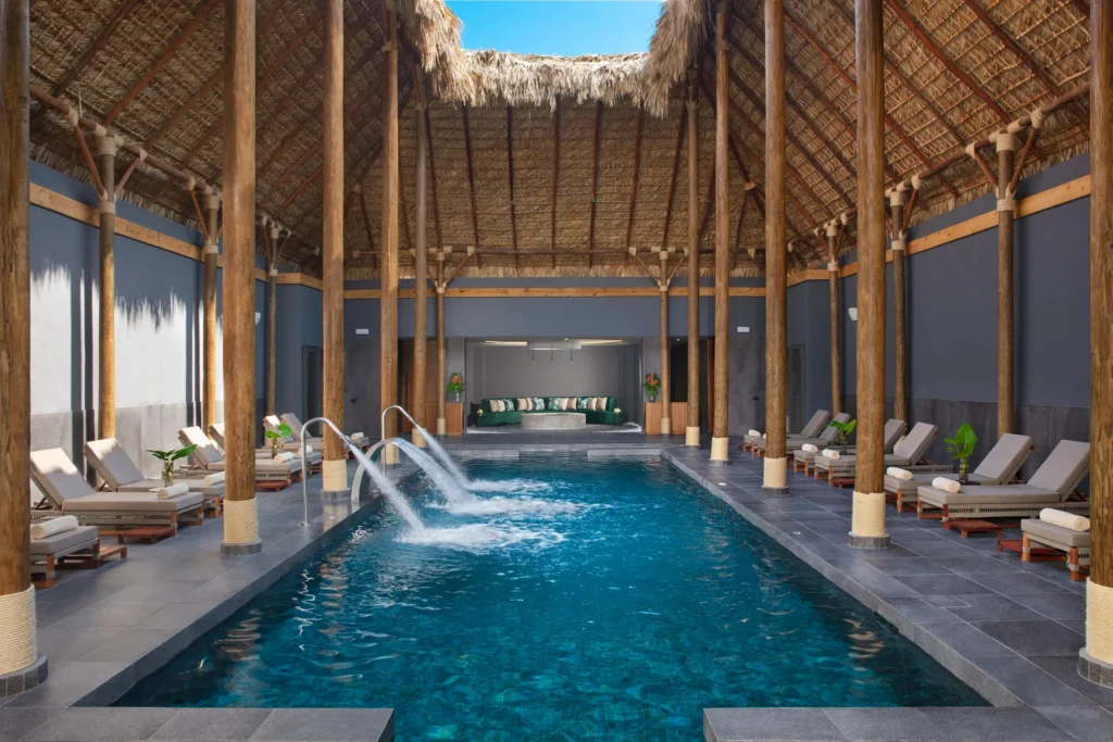 Indoor hydrotherapy pool with loungers and thatched ceiling at Dreams Flora Resort & Spa Punta Cana spa.