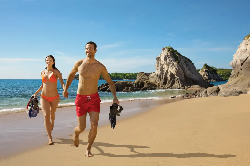 Couple walking along the beach with snorkeling gear at Dreams Huatulco Resort & Spa.