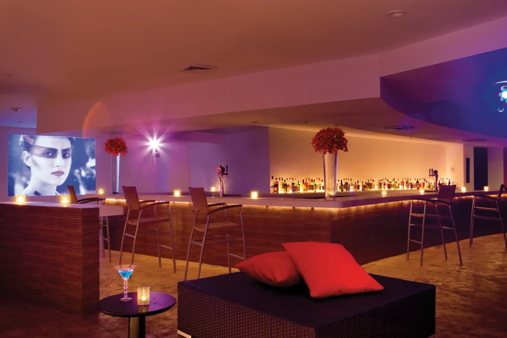 Desires Music Lounge Bar at Dreams Huatulco Resort & Spa featuring a sleek indoor bar, DJ lighting, modern lounge seating, and vibrant nightlife ambiance.