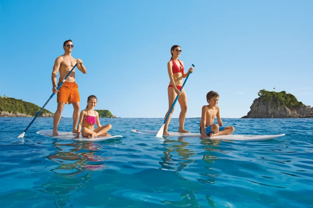 Family paddleboarding together in calm ocean waters at Dreams Huatulco Resort & Spa in Huatulco, Mexico.