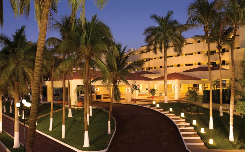 Resort entrance and lobby illuminated at night at Dreams Huatulco Resort & Spa with palm-lined pathways.