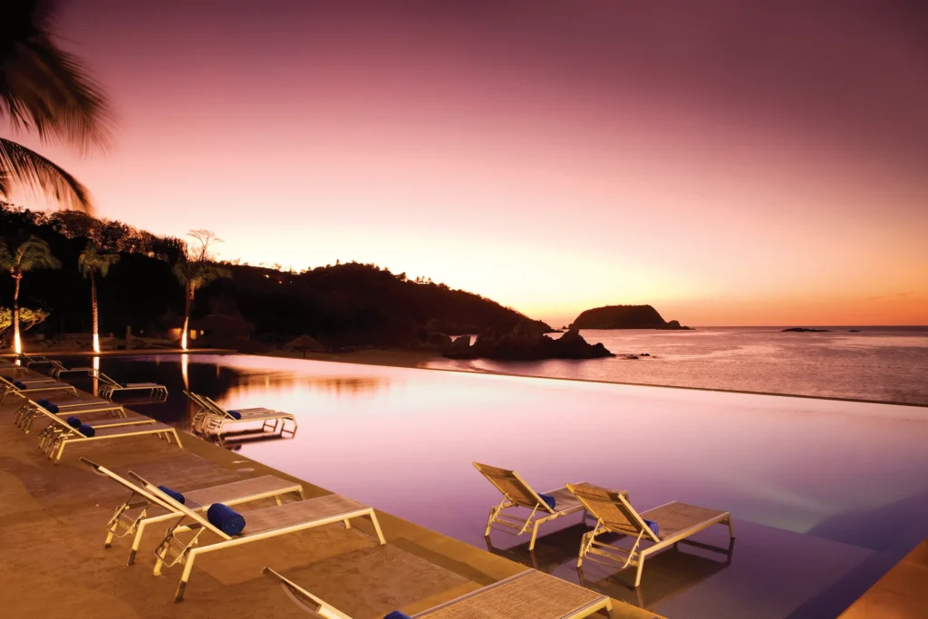 Infinity pool at sunset at Dreams Huatulco Resort & Spa with ocean views and in-pool loungers overlooking the Pacific.
