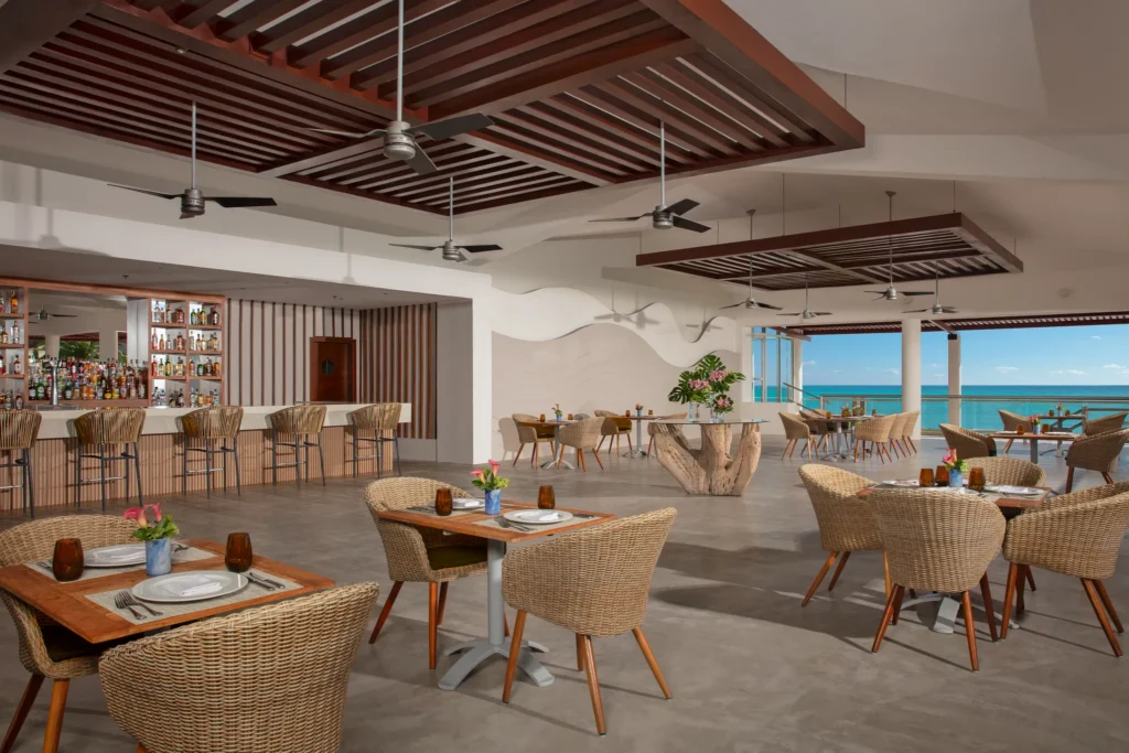 Castaways poolside restaurant at Dreams Jade Resort & Spa featuring open-air ocean views, wicker seating, and a full-service bar.