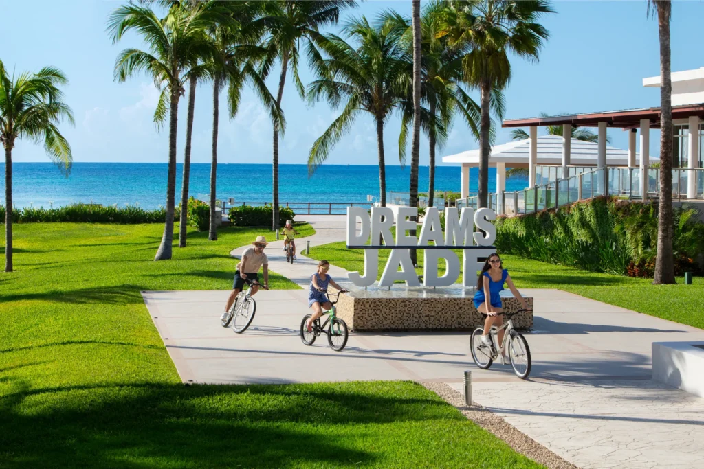 Family riding bicycles near the Dreams Jade Resort & Spa oceanfront entrance.