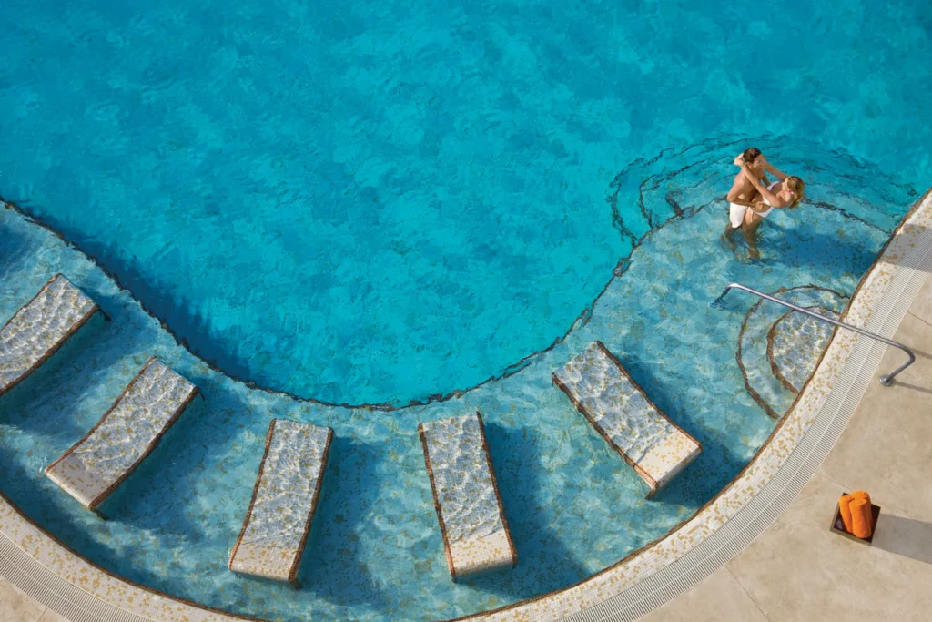 Couple relaxing in the infinity pool at Dreams Jade Resort & Spa overlooking the Caribbean Sea.