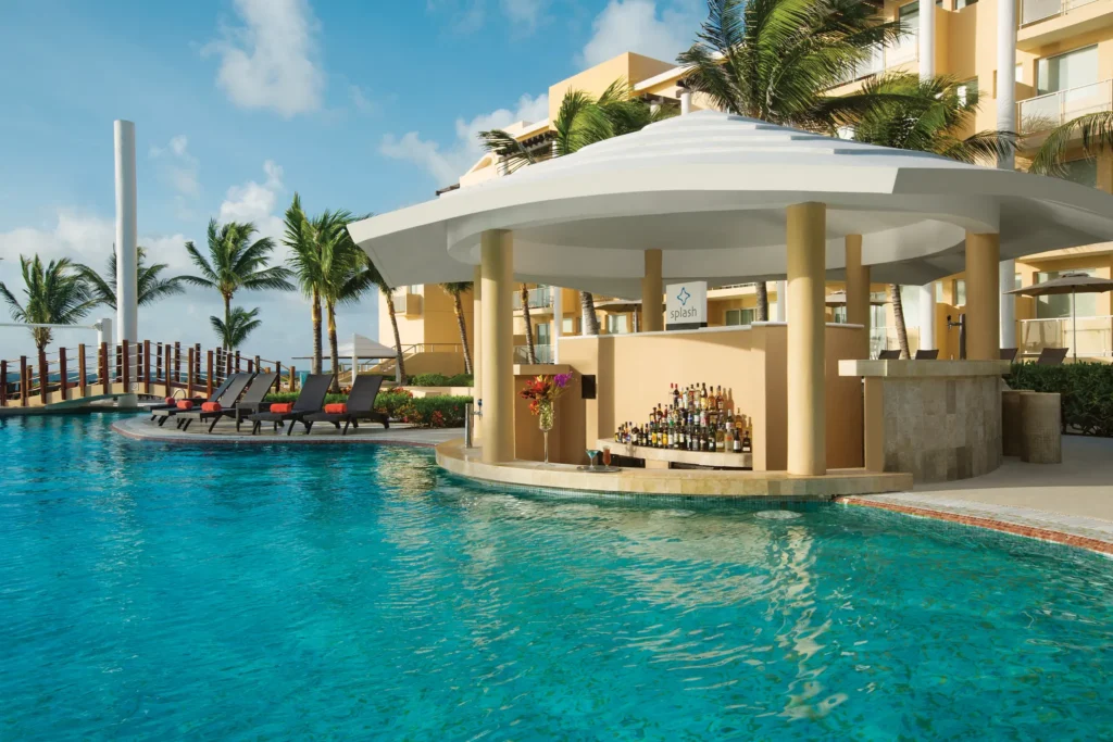 Splash swim-up pool bar at Dreams Jade Resort & Spa featuring tropical cocktails, palm trees, and the main resort pool.