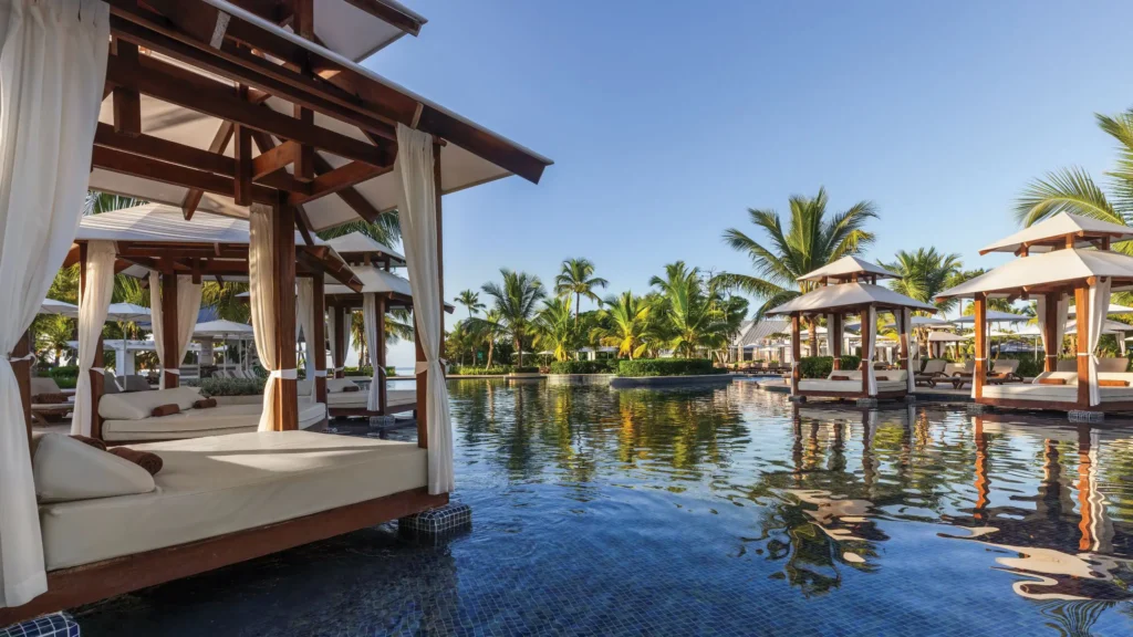 Elegant pool cabanas surrounded by palm trees at Dreams La Romana Resort & Spa overlooking a tranquil Caribbean-style pool.