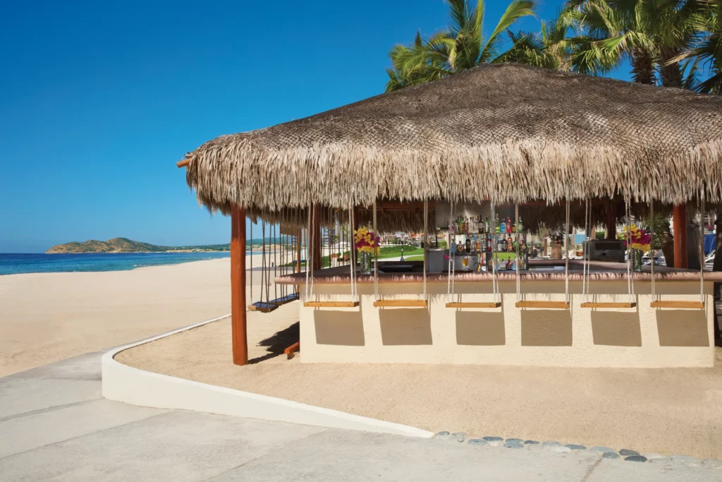 Barefoot Grill beach bar at Dreams Los Cabos Suites Golf Resort & Spa featuring a thatched-roof bar with swing seats and oceanfront views.