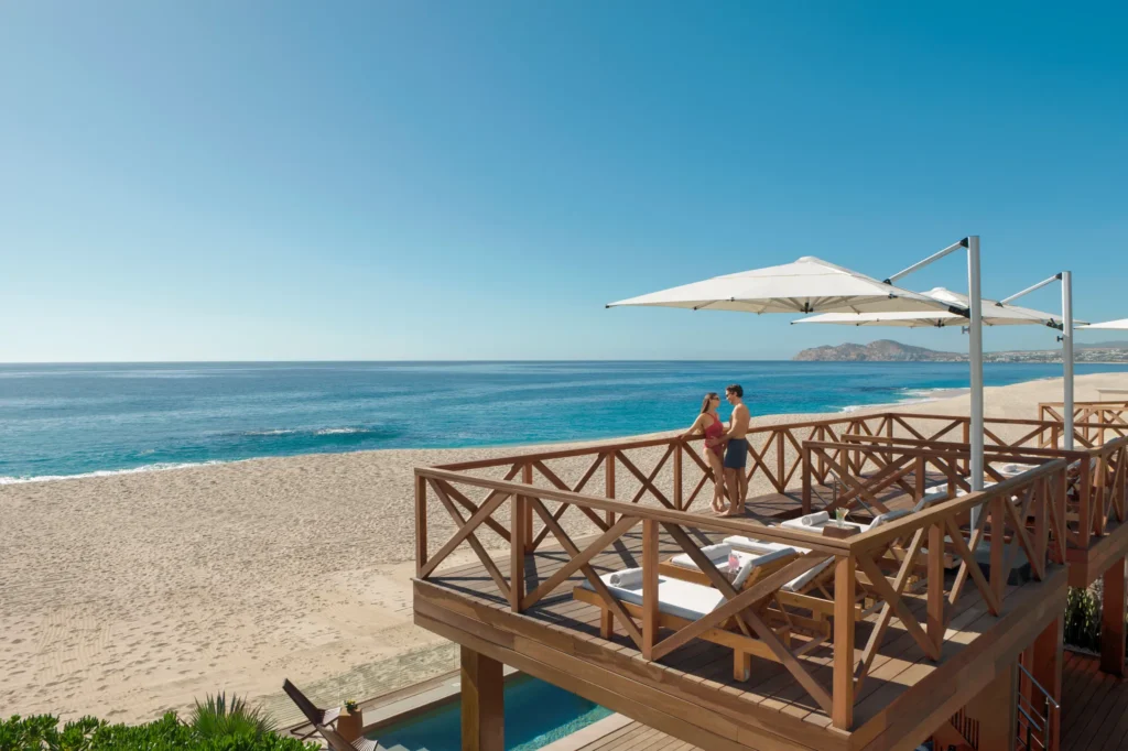Couple standing on a luxury beach cabana deck overlooking the Sea of Cortez at Dreams Los Cabos Suites Golf Resort & Spa.
