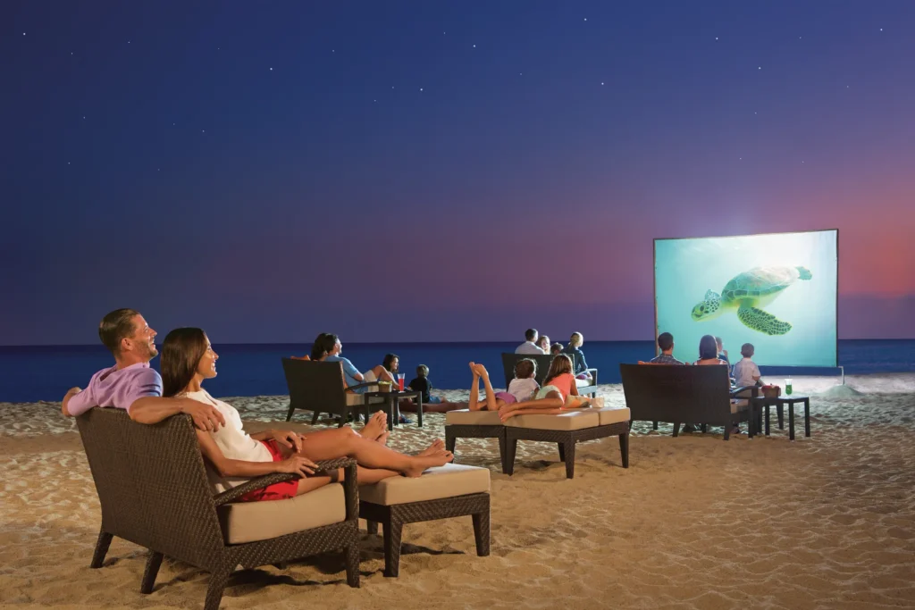 Guests watching an outdoor movie on the beach at night at Dreams Los Cabos Suites Golf Resort & Spa.