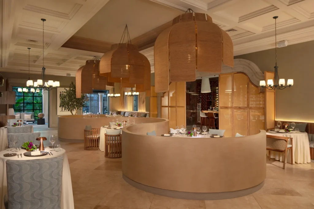 Bordeaux French restaurant dining room at Dreams Los Cabos Suites Golf Resort & Spa featuring elegant curved booths, woven pendant lighting, and an intimate adults-only atmosphere.