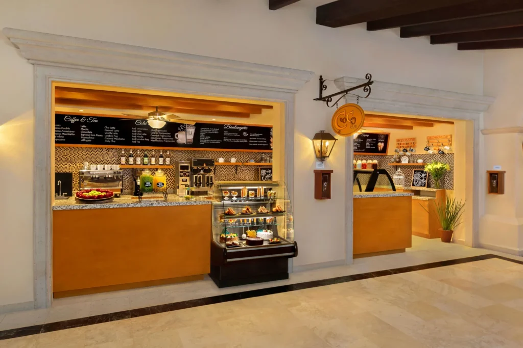 Coco Café coffee shop at Dreams Los Cabos Suites Golf Resort & Spa featuring espresso drinks, pastries, and deli snacks at a casual grab-and-go café counter.