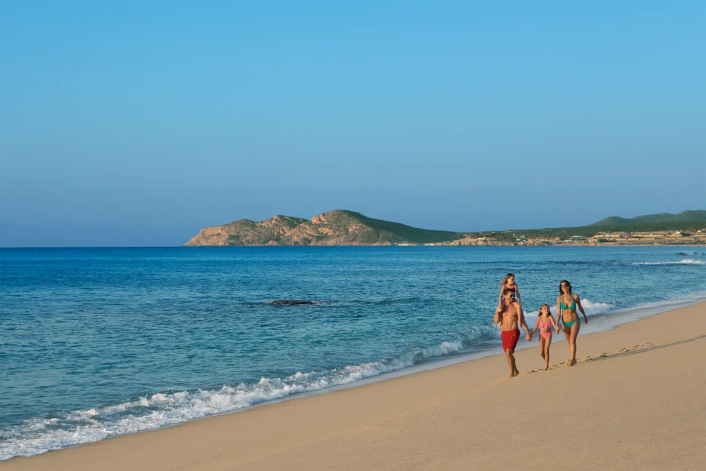 Family walking together along the sandy beach at Dreams Los Cabos Suites Golf Resort & Spa in Los Cabos.