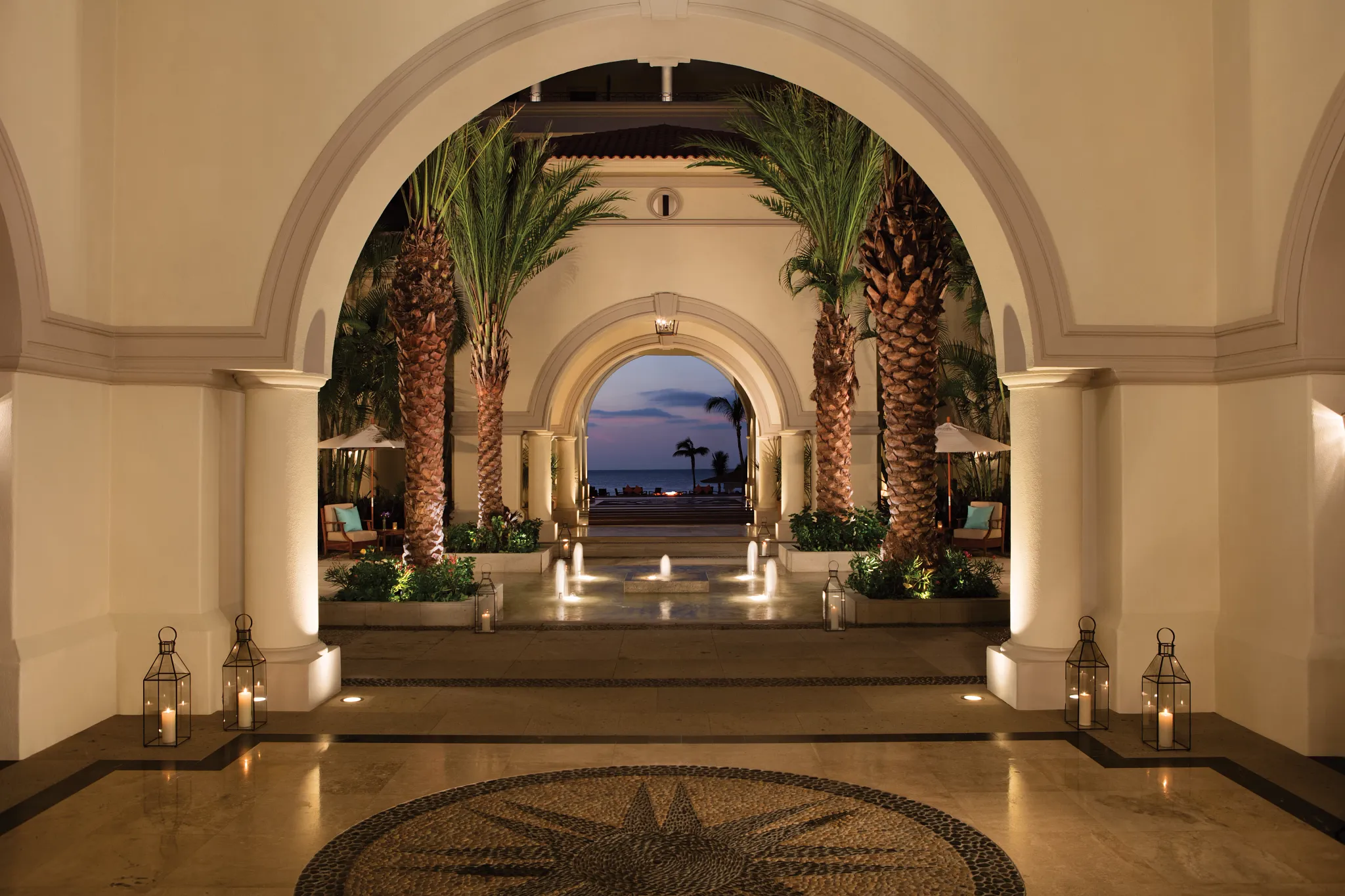 Grand arched lobby entrance with palm trees and ocean view at Dreams Los Cabos Suites Golf Resort & Spa.