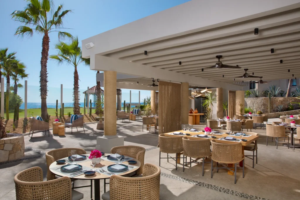 Oceana seafood restaurant at Dreams Los Cabos Suites Golf Resort & Spa featuring open-air oceanfront dining with woven chairs, palm trees, and Sea of Cortez views.