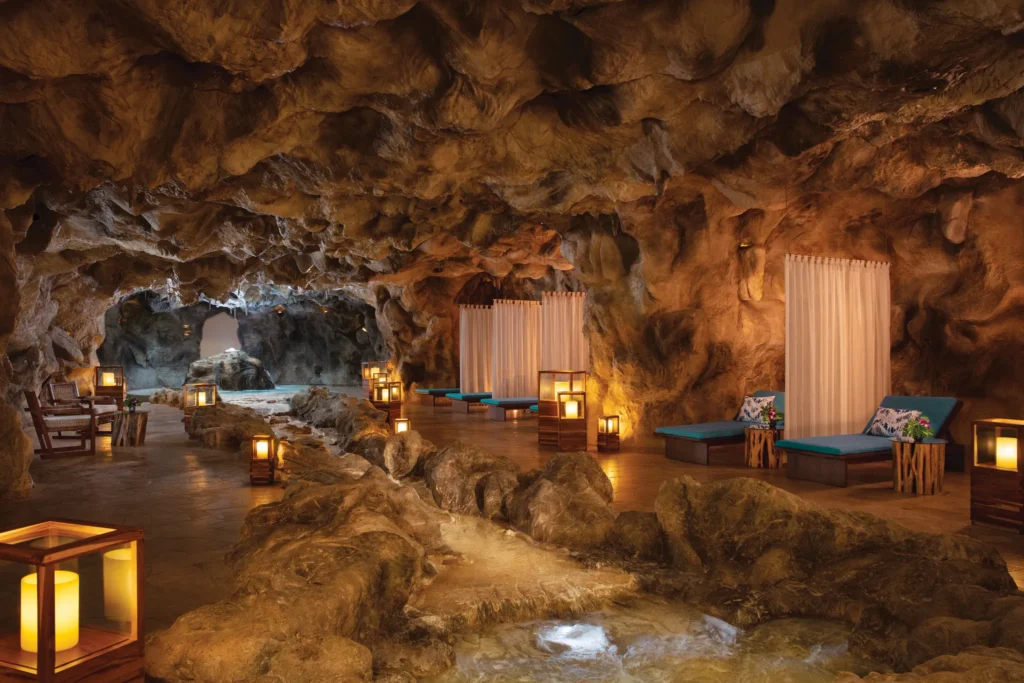 Cave-style cenote spa lounge with candlelight, loungers, and natural rock formations at Dreams Natura Resort & Spa.