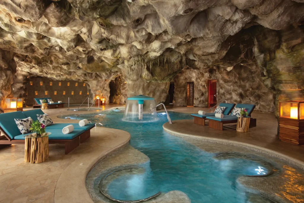 Indoor hydrotherapy pool with loungers and waterfall features inside a cave spa at Dreams Natura Resort & Spa.