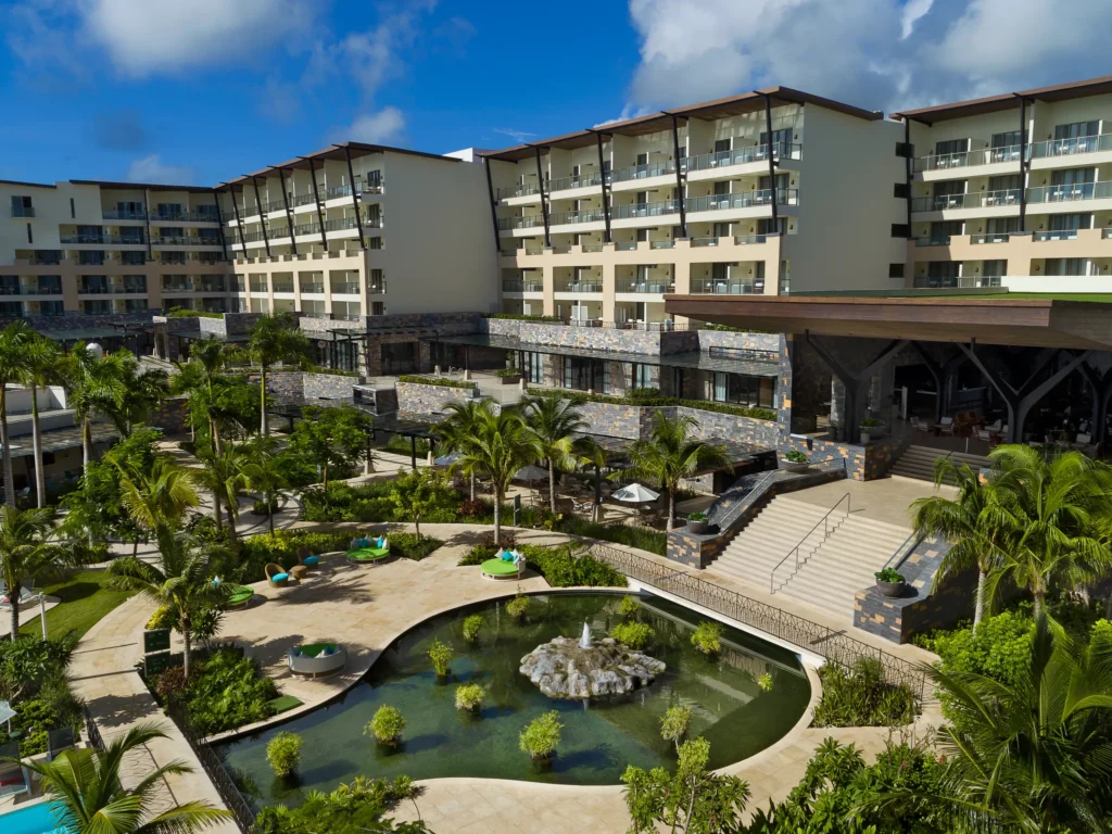 Landscaped gardens with pond, palm trees, and resort buildings at Dreams Natura Resort & Spa in Riviera Cancun.