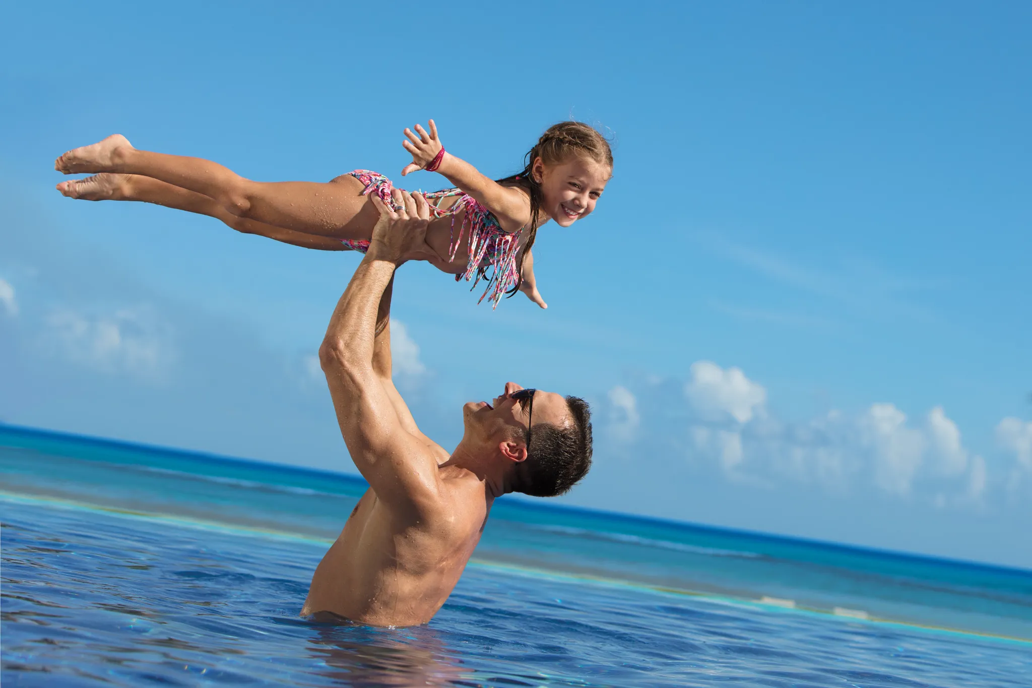 Father lifting his daughter above the ocean water at Dreams Onyx Resort & Spa beach in Punta Cana.