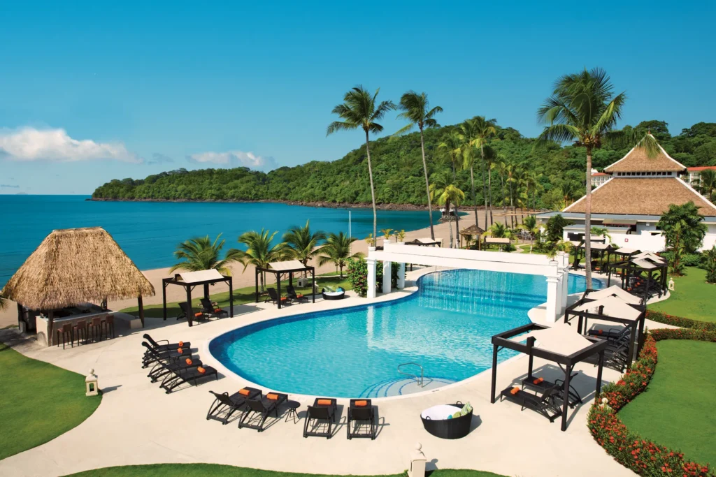 Oceanfront adults-only pool with cabanas and palm trees at Dreams Playa Bonita Panama, offering a serene beachfront escape.